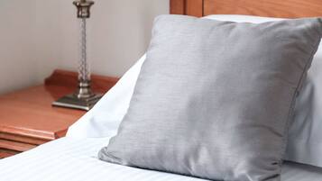 Een net opgemaakt bed met een grijs kussen en een wit kussen, een houten nachtkastje met een lamp, en een houten hoofdbord.