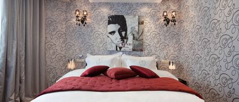 A bedroom with a large bed, patterned wallpaper, and wall sconces.