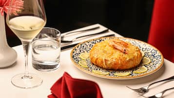 Une assiette avec une pâtisserie, un verre d’eau et un verre de vin blanc, posés sur une table recouverte d’une serviette rouge et agrémentée de couverts.