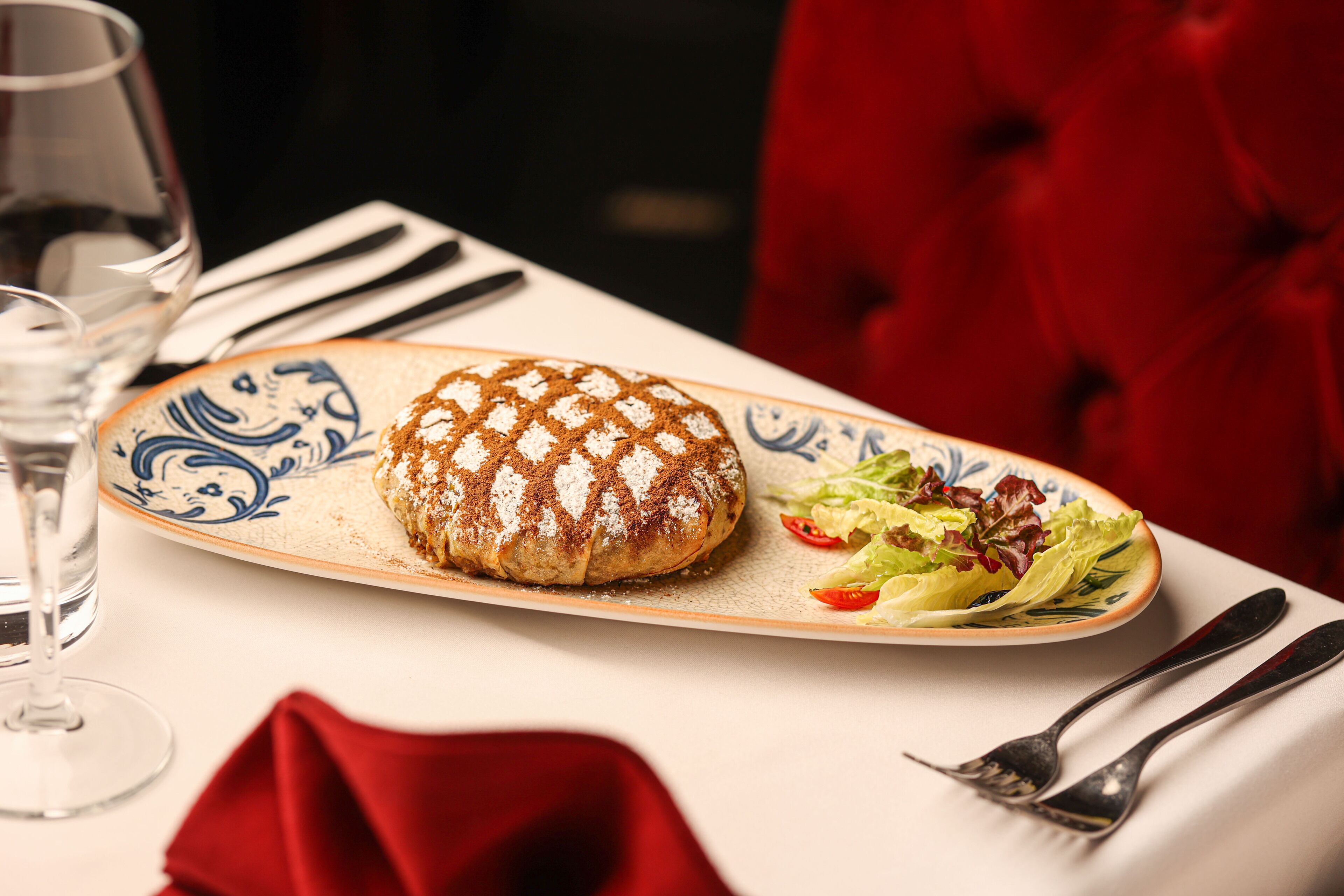 Un plato con un pastel horneado y ensalada sobre una mesa con servilleta roja y cubiertos.