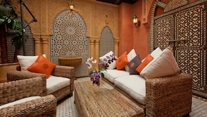 A cozy seating area with wicker furniture, a decorative wall with intricate patterns, and a large ornate window.