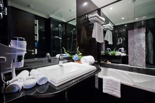 Un baño moderno con un espejo grande, un lavamanos blanco, una bañera y toallas ordenadas.