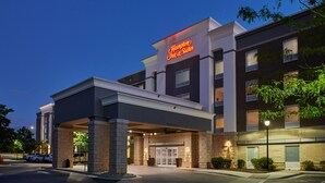 Un hôtel Hampton Inn & Suites doté d’une entrée moderne, d’une façade en briques et d’une enseigne lumineuse.