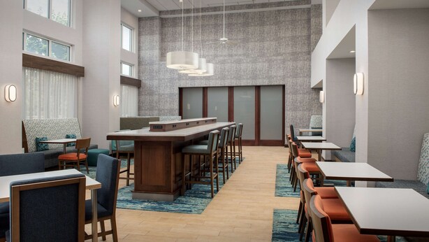 Un hall d’hôtel moderne doté d’un long comptoir, de plusieurs espaces salon et d’un plafond haut avec des luminaires suspendus.