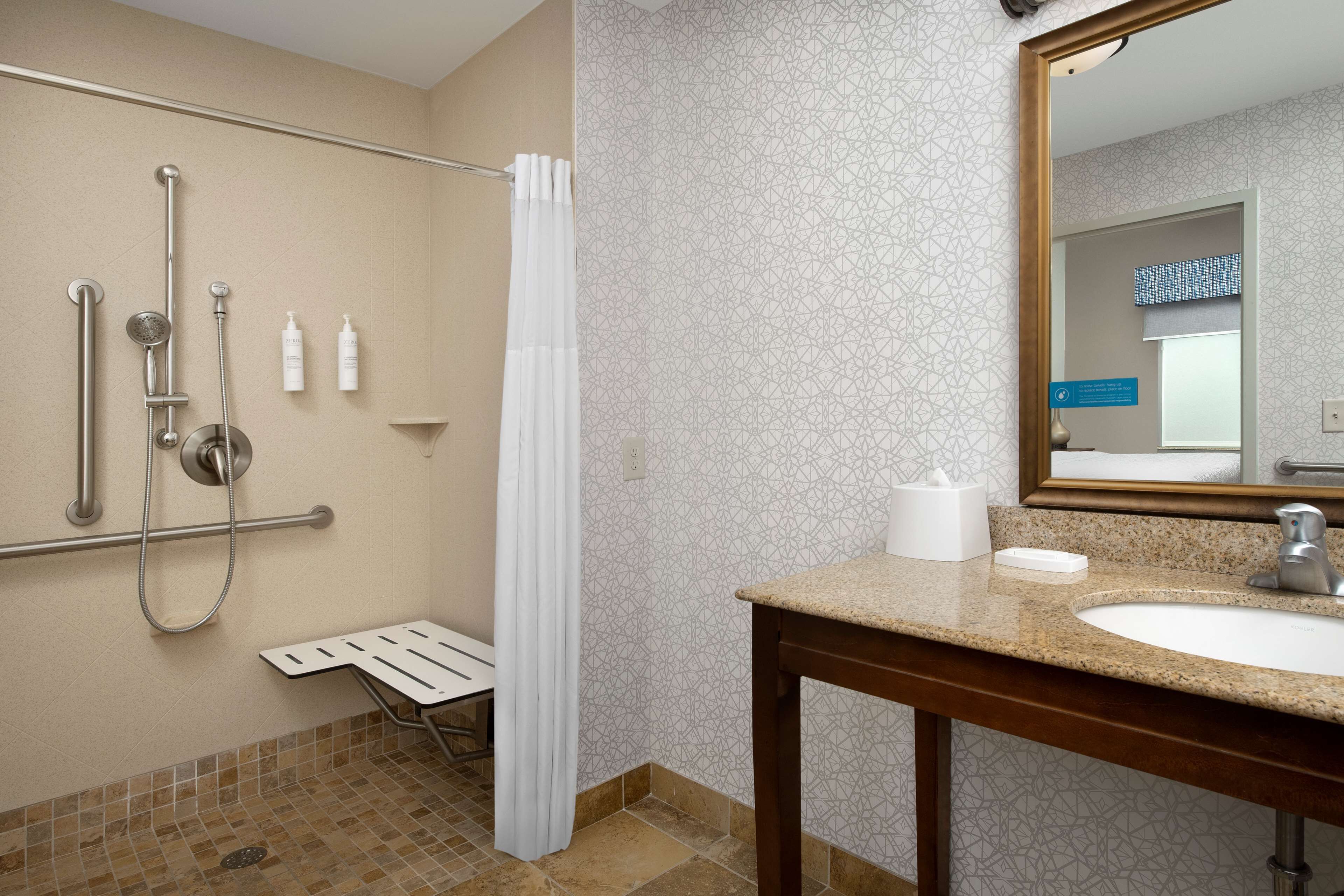 A bathroom with a shower, grab bar, sink, and mirror.
