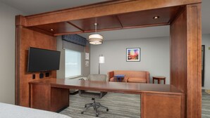 Une chambre d’hôtel avec un bureau en bois, un téléviseur à écran plat, un fauteuil confortable, un canapé et une petite table.