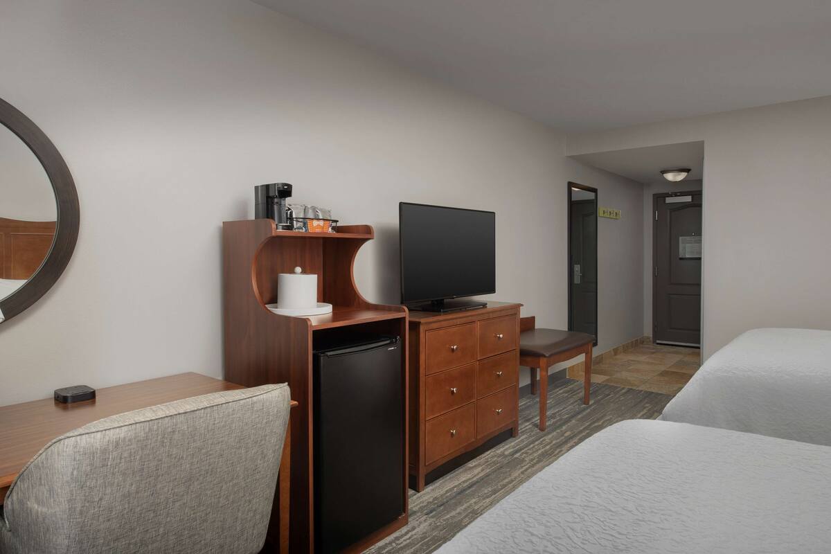 A hotel room with a bed, a desk with a television, a refrigerator, a chair, and a mirror.