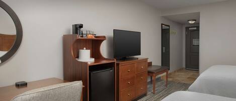 Una habitación de hotel con cama, escritorio con televisor, refrigerador, silla y espejo.