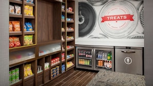 Un présentoir proposant divers types de chips et d’en-cas, un rayon réfrigéré avec des boissons, et une fresque murale faisant la publicité de produits sucrés.