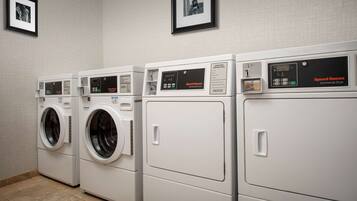 A row of Speed Queen commercial dryers in a laundry room with tiled flooring and framed pictures on the wall.