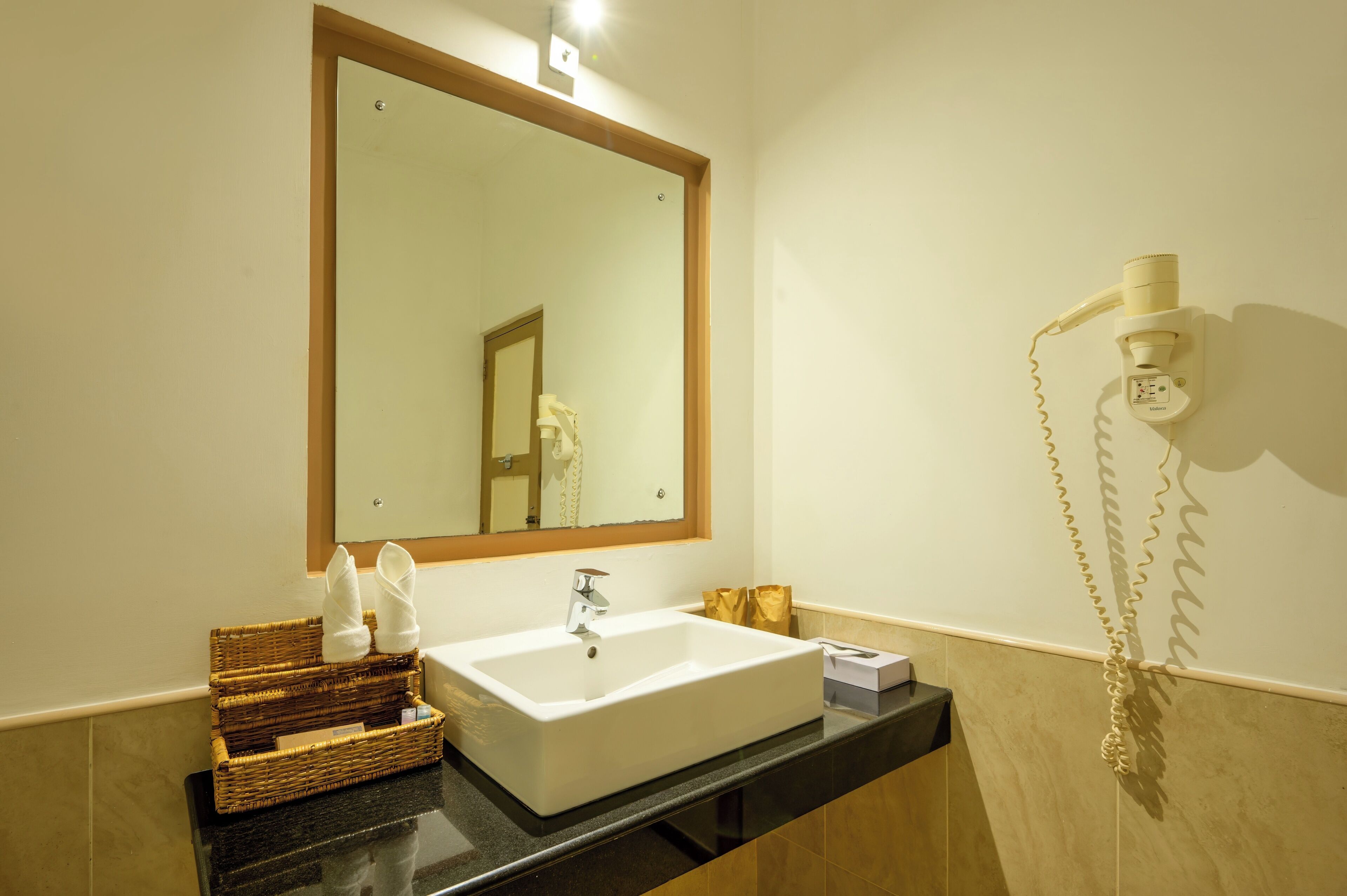 A bathroom with a white sink, a mirror, and a hairdryer mounted on the wall.