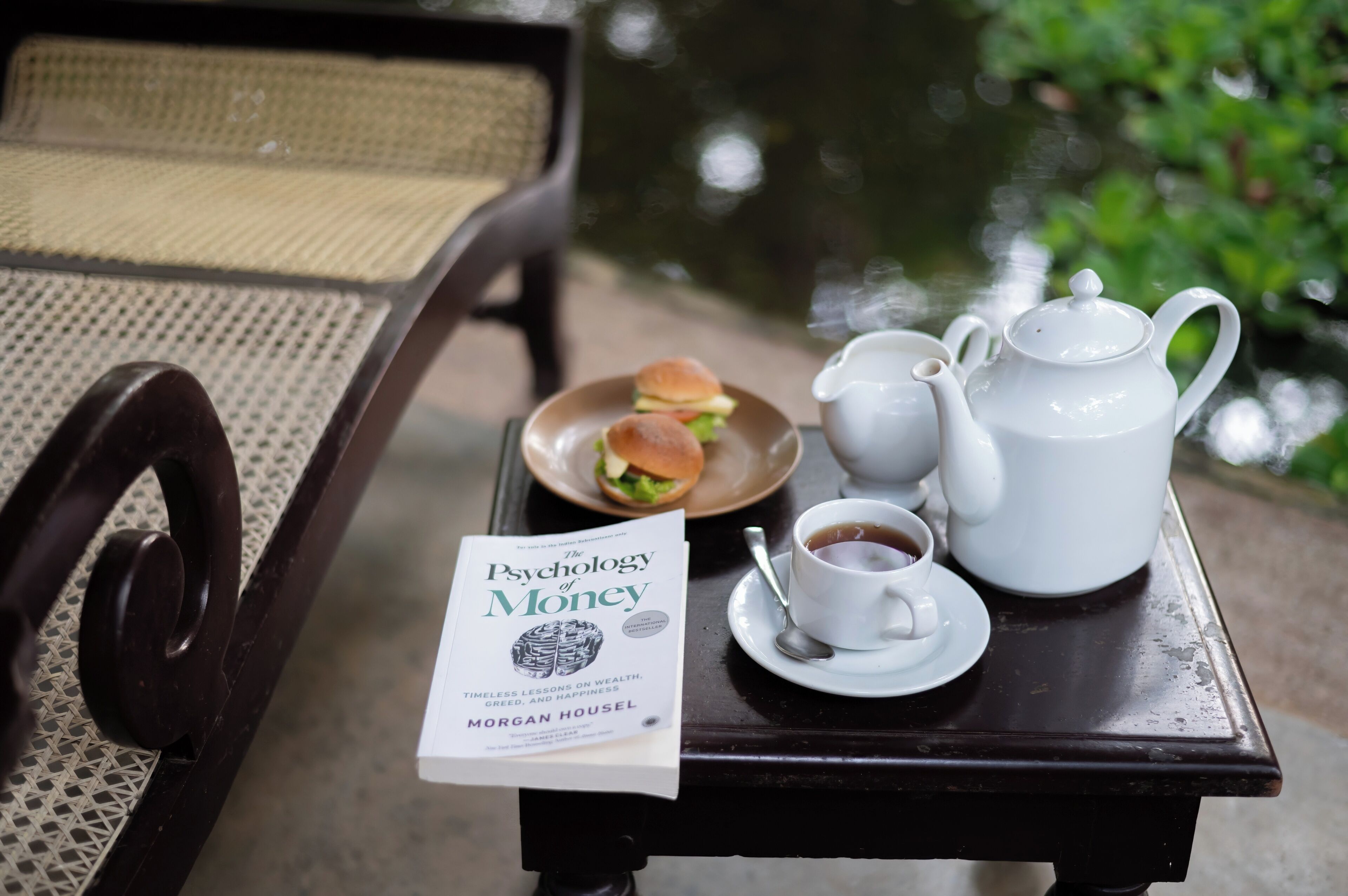 A table with a book titled "The Psychology of Money," a teapot, cups, and a plate with sandwiches.