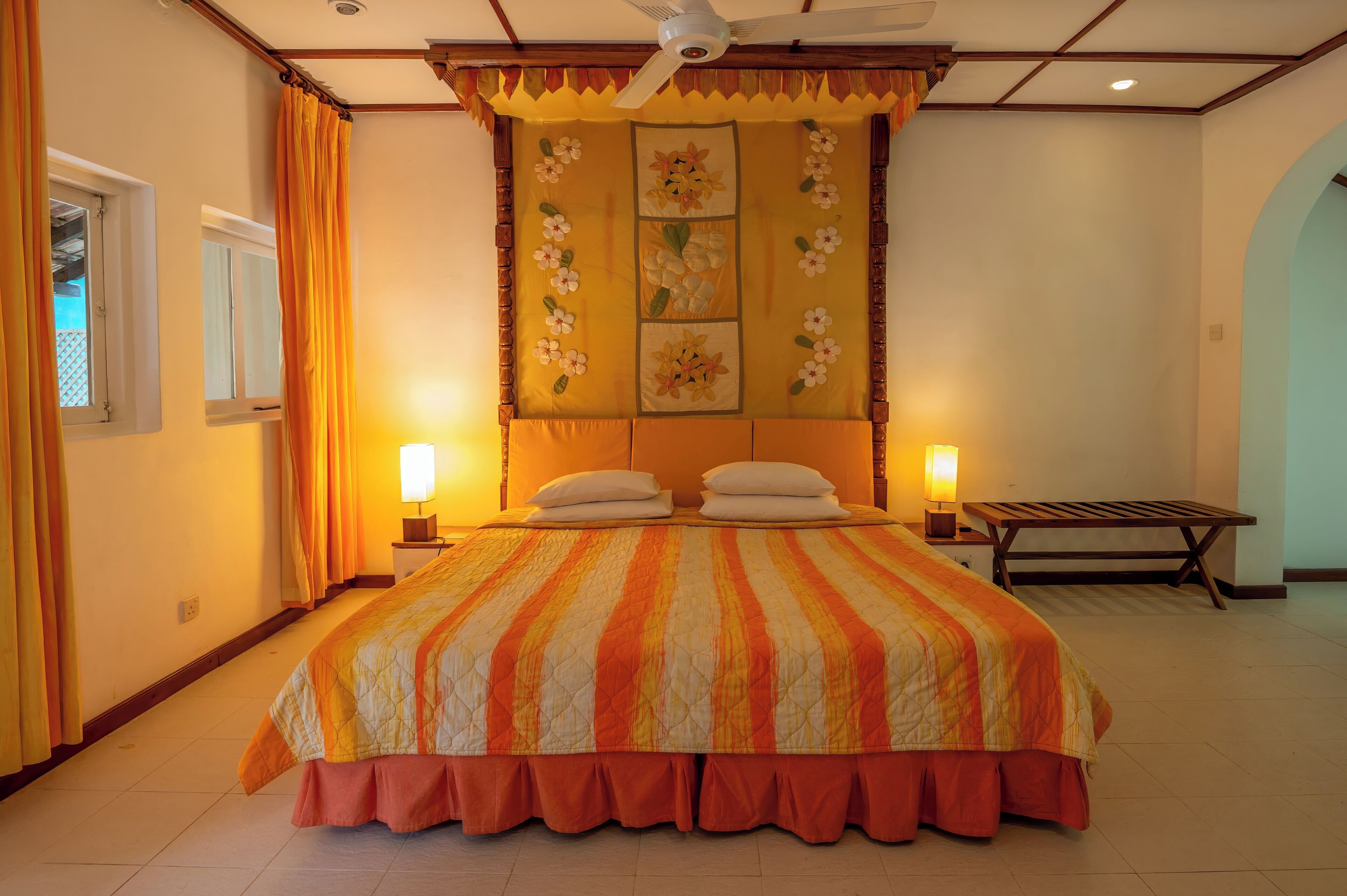 Une chambre d’hôtel avec un grand lit, deux lampes de chevet, un ventilateur de plafond et un élément décoratif mural.