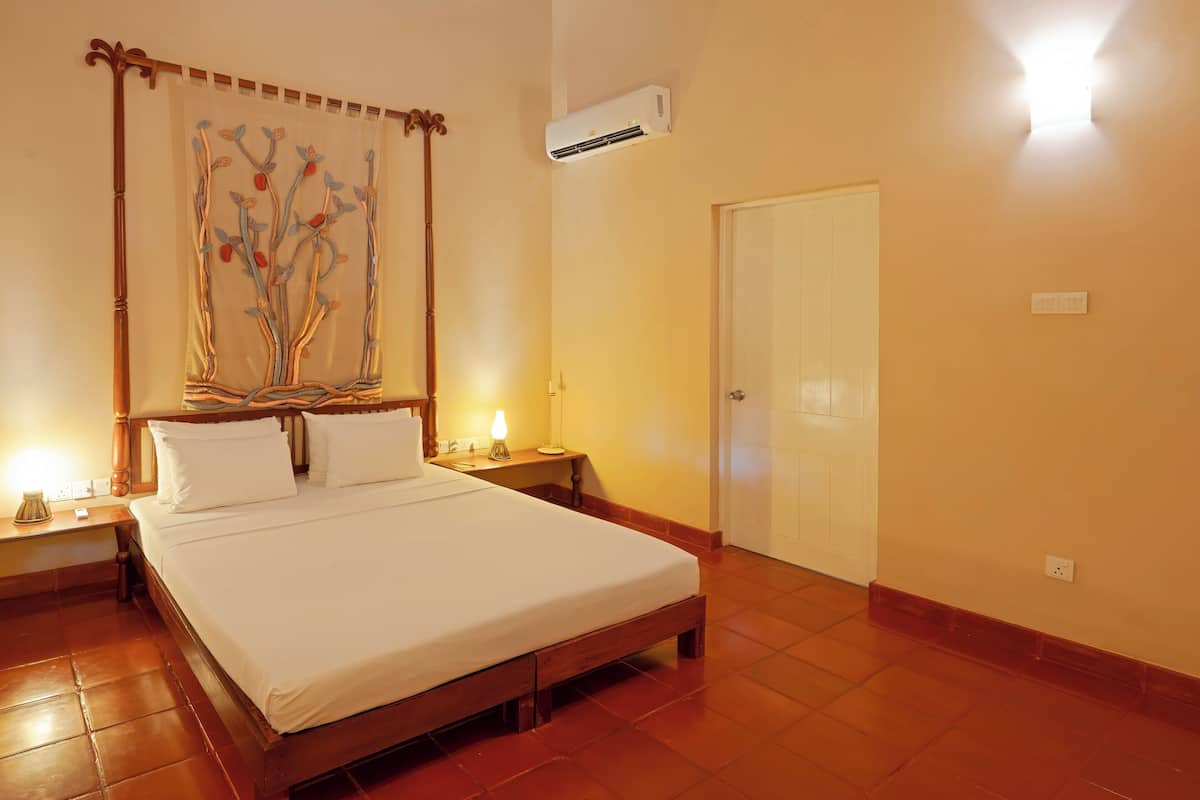A bedroom with a wooden bed, a nightstand with a lamp, a wall-mounted air conditioner, and a door.