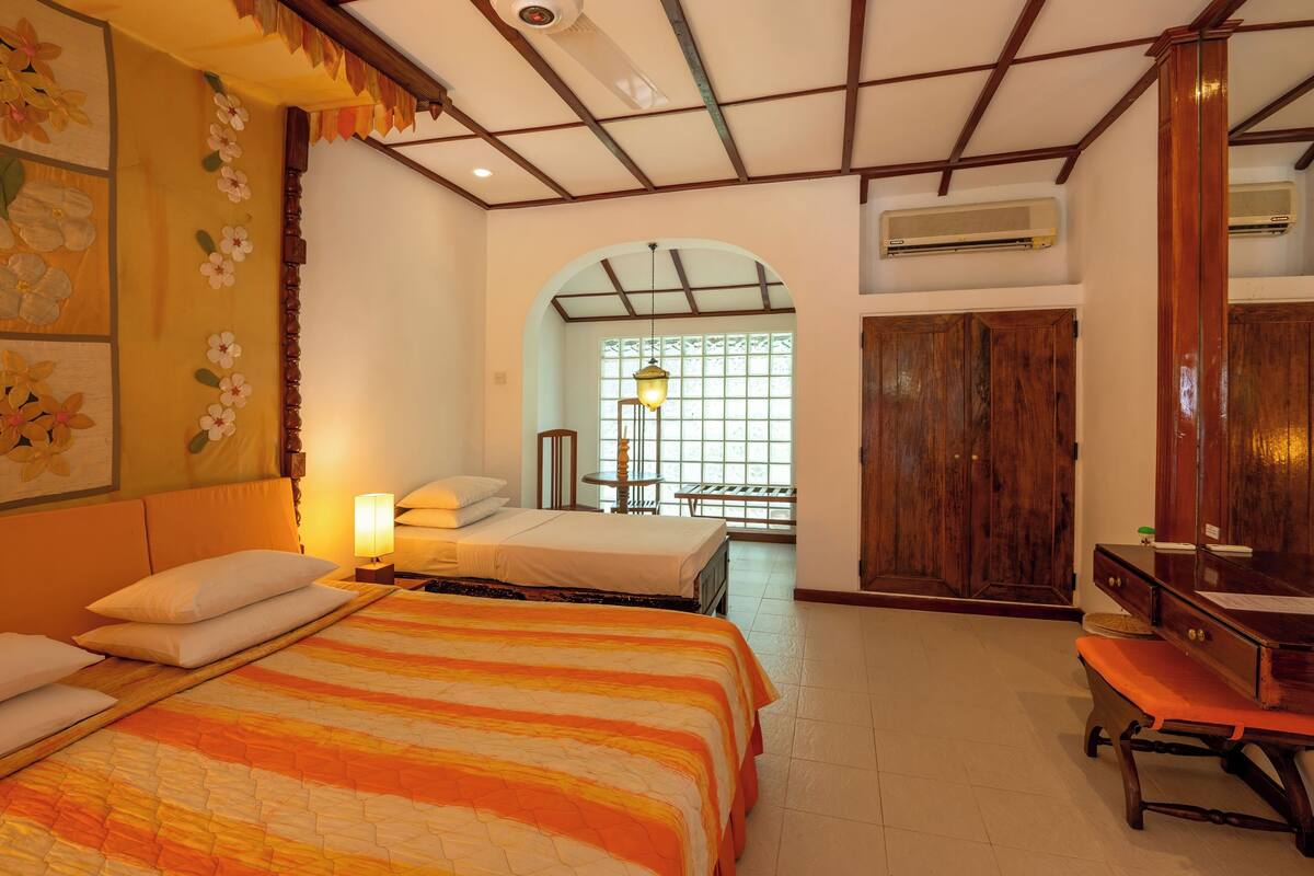 A hotel room with two beds, a wooden bench, a desk, and a large window with a view.