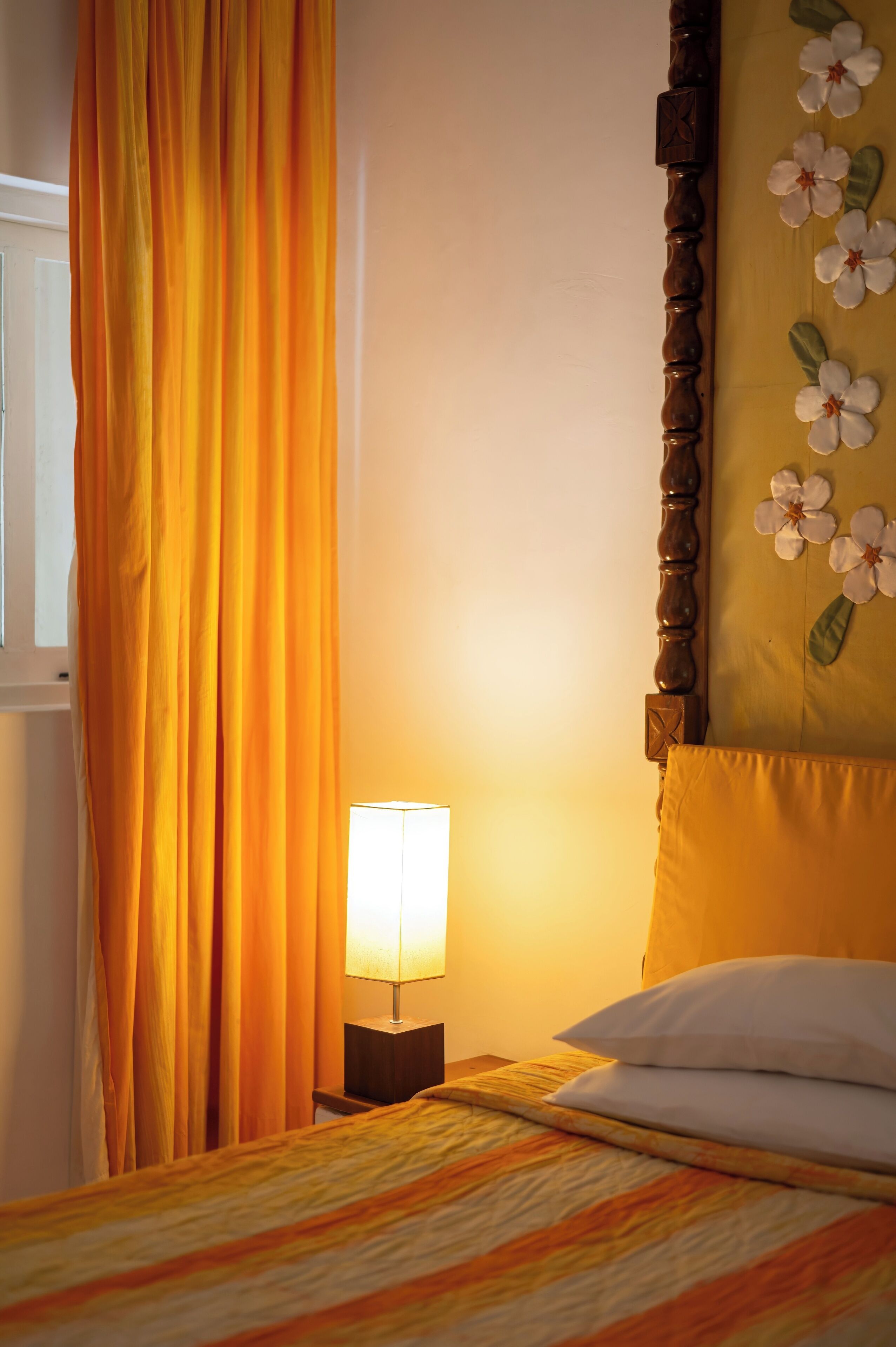 A bed with a striped bedspread, a bedside lamp, and a floral wall decoration.