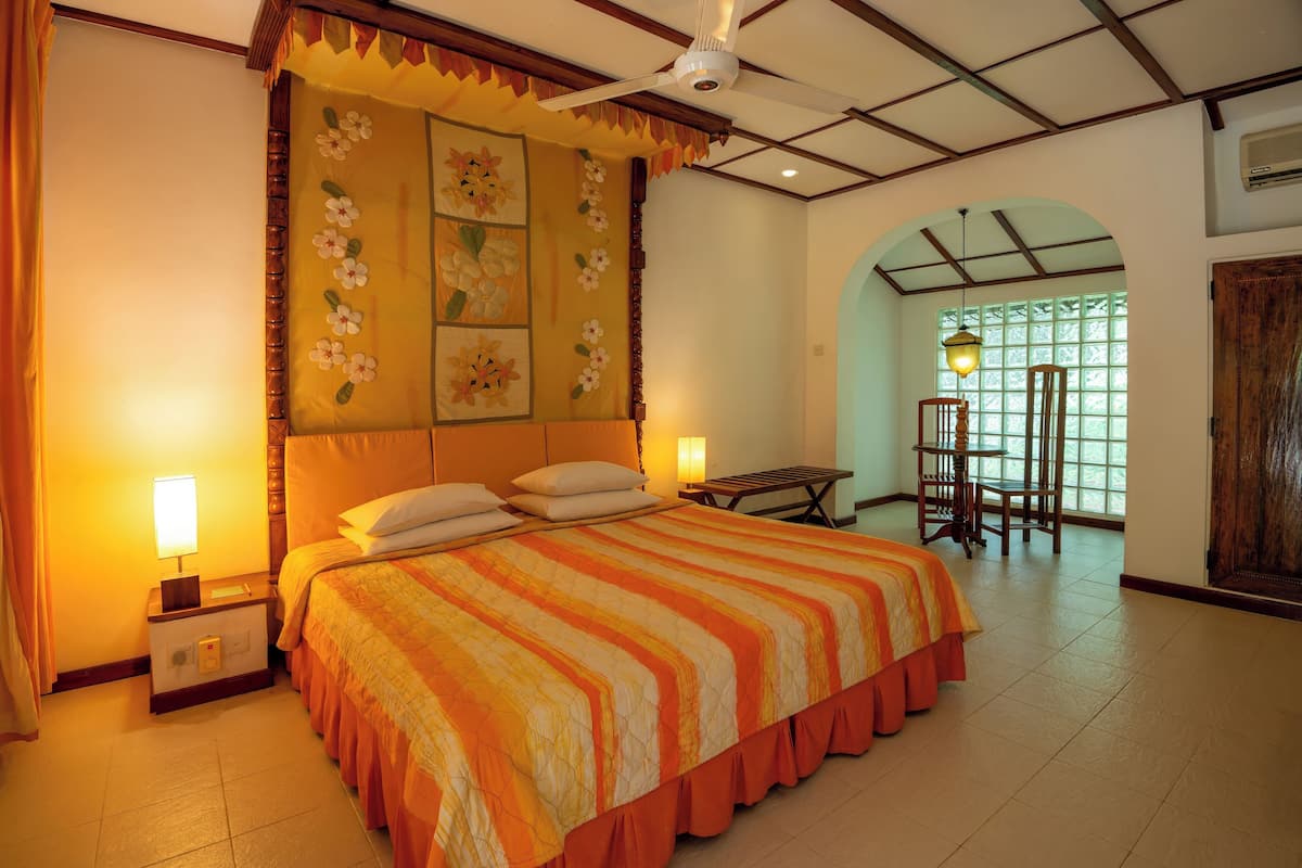 A hotel room with a large bed, a nightstand, a desk, and a chair. There is a window with a view of greenery outside.