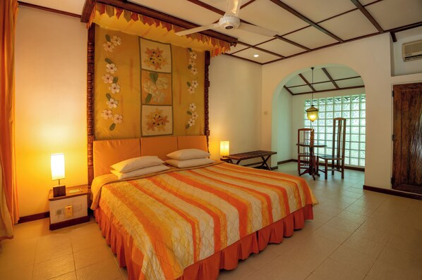 Habitación de hotel con una cama grande, una mesita de noche con lámpara, un ventilador de techo y una ventana con vistas al exterior.