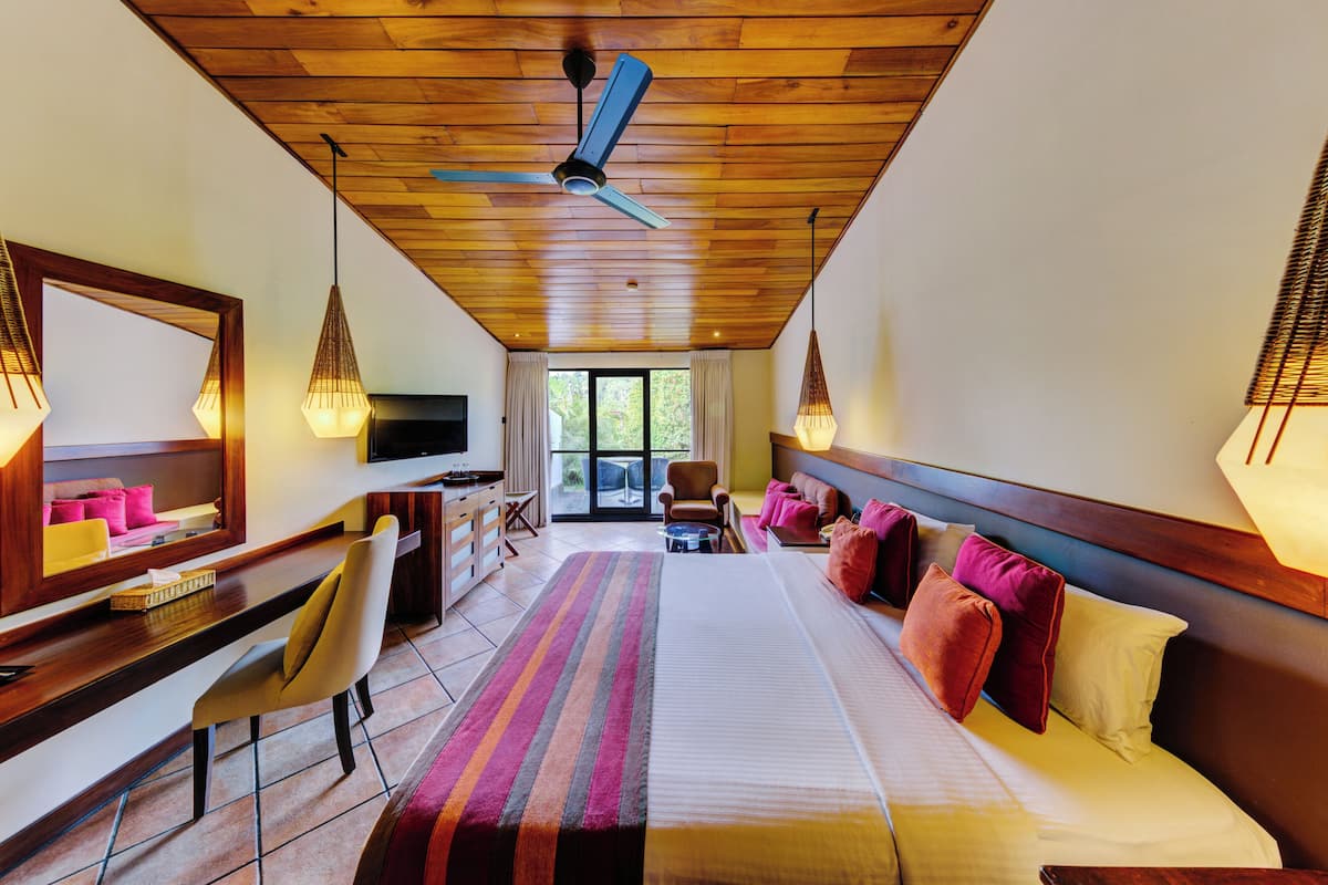 Une chambre d’hôtel équipée d’un lit, d’un bureau, d’une chaise, d’une télévision et d’un ventilateur de plafond.