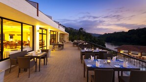 An outdoor dining area with tables and chairs, overlooking a river and hills. - Cinnamon Citadel Kandy (Kandy)