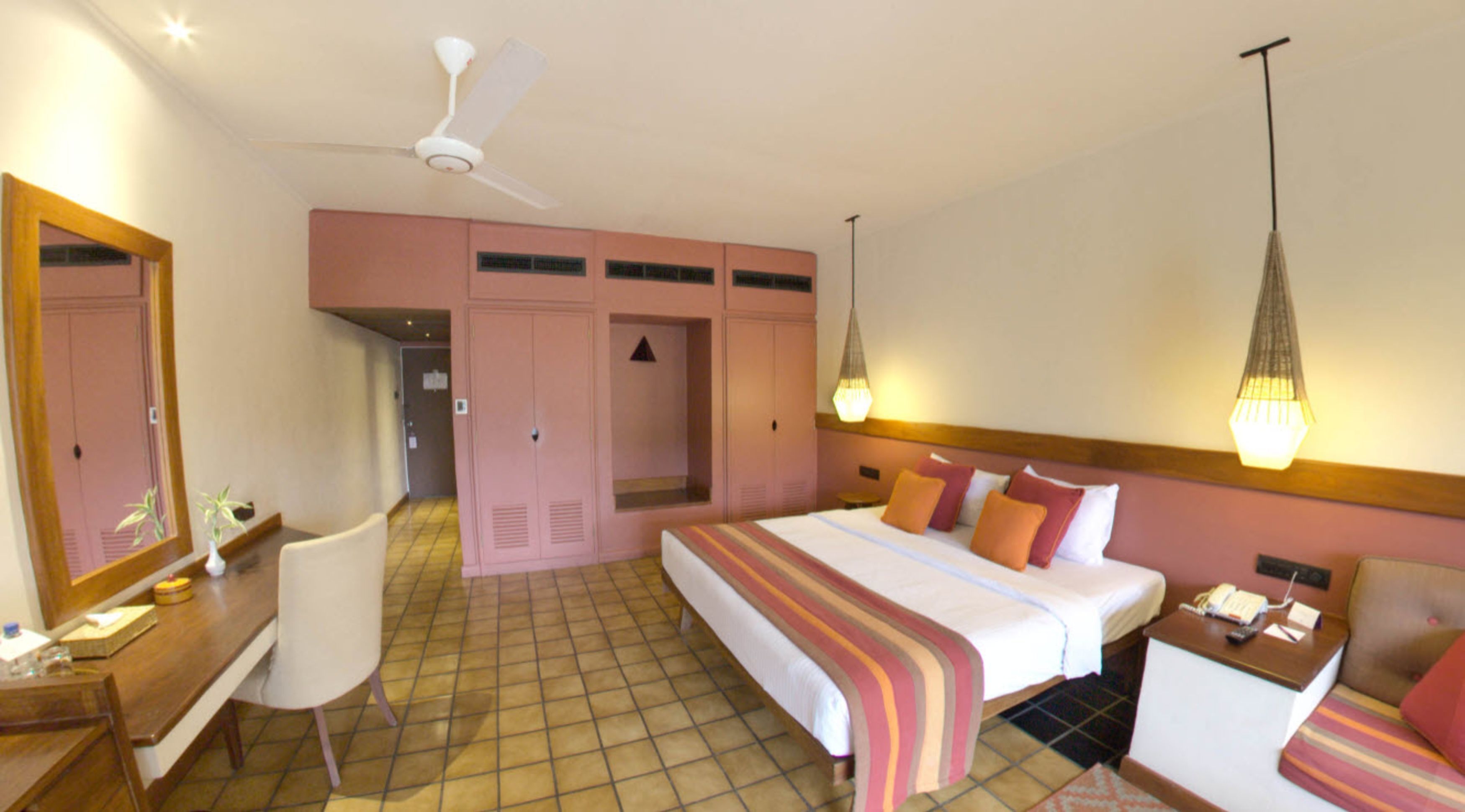A hotel room with a bed, bedside table, chair, wardrobe, and a ceiling fan.