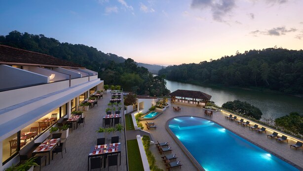 A hotel with outdoor dining and a swimming pool, surrounded by lush greenery and a river. - Cinnamon Citadel Kandy (Kandy)