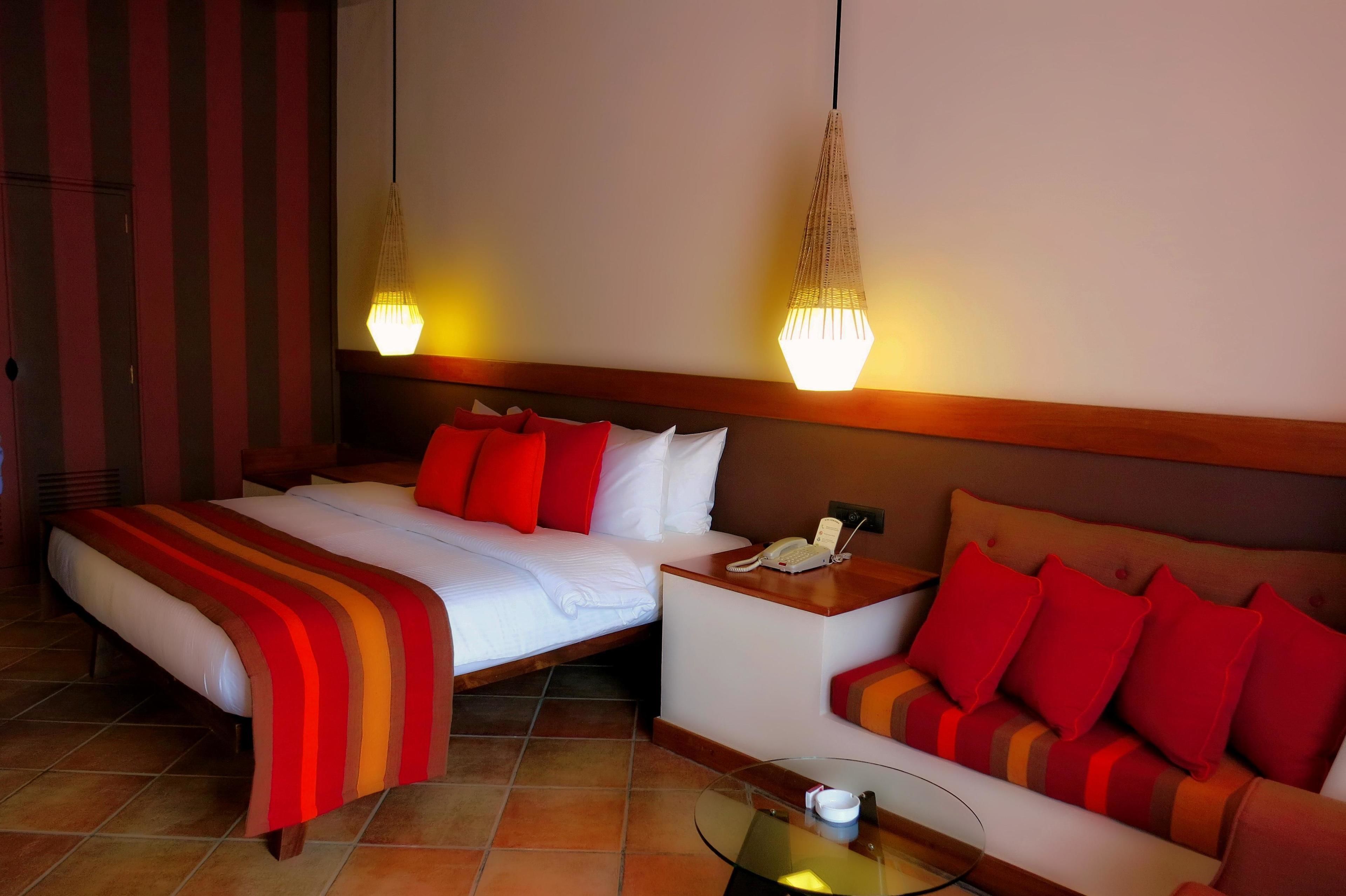 A hotel room with a bed, a sofa, a bedside table with a phone, and two hanging lamps.