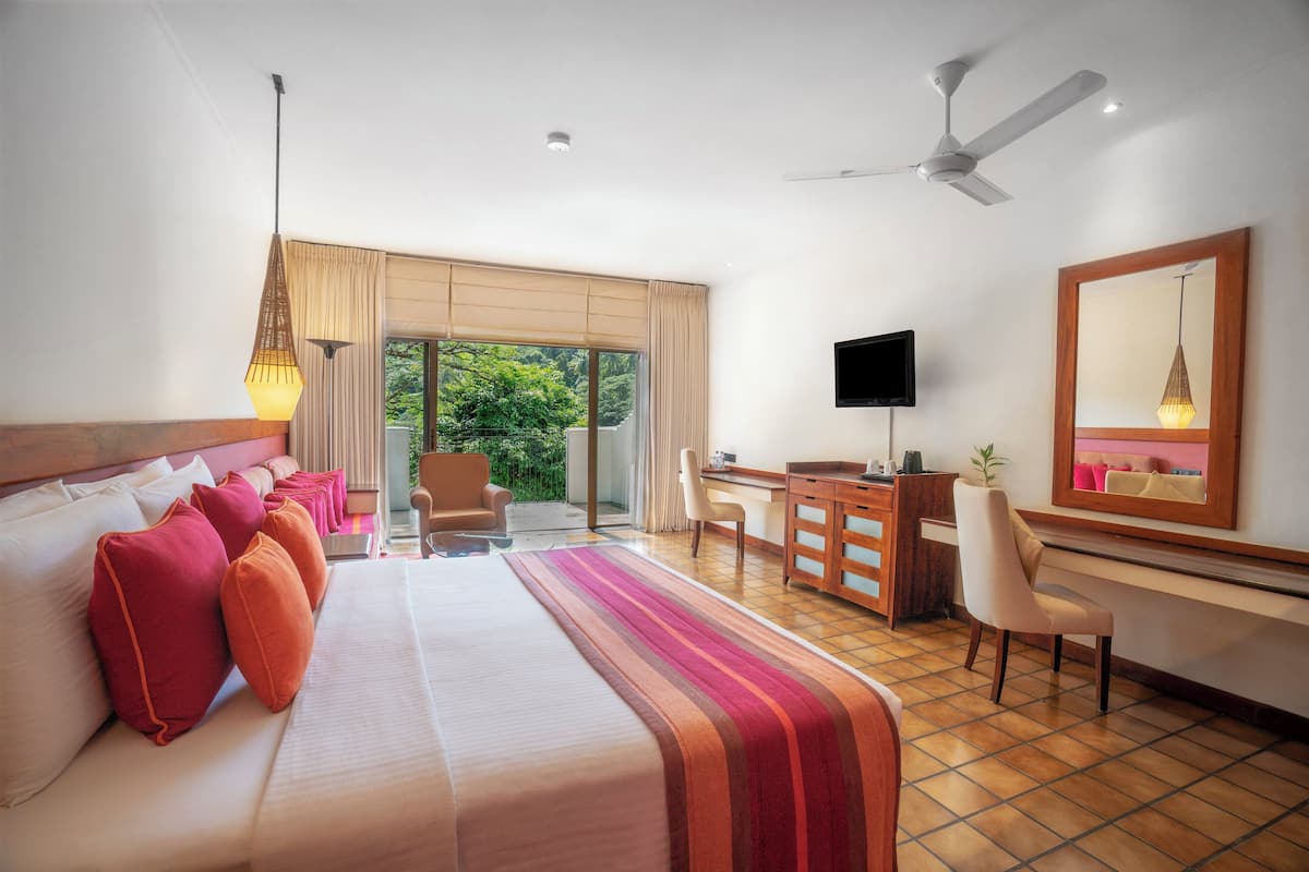 Une chambre d’hôtel avec un grand lit, un bureau, une chaise, une télévision et un ventilateur de plafond.