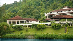 A hotel with a large building and a smaller structure with a red roof, surrounded by lush greenery and a body of water. - Cinnamon Citadel Kandy (Kandy)