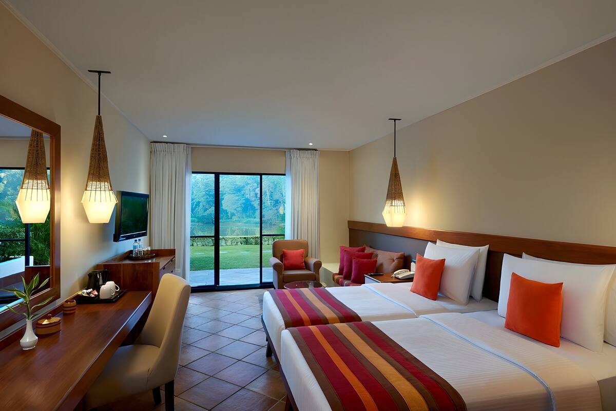 Une chambre d’hôtel avec deux lits, un bureau, une chaise, une télévision et un balcon donnant sur l’extérieur.