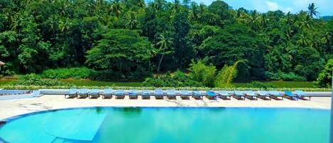 A swimming pool with lounge chairs and a tropical forest backdrop.