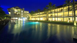 A hotel with a swimming pool, multiple floors, and palm trees.