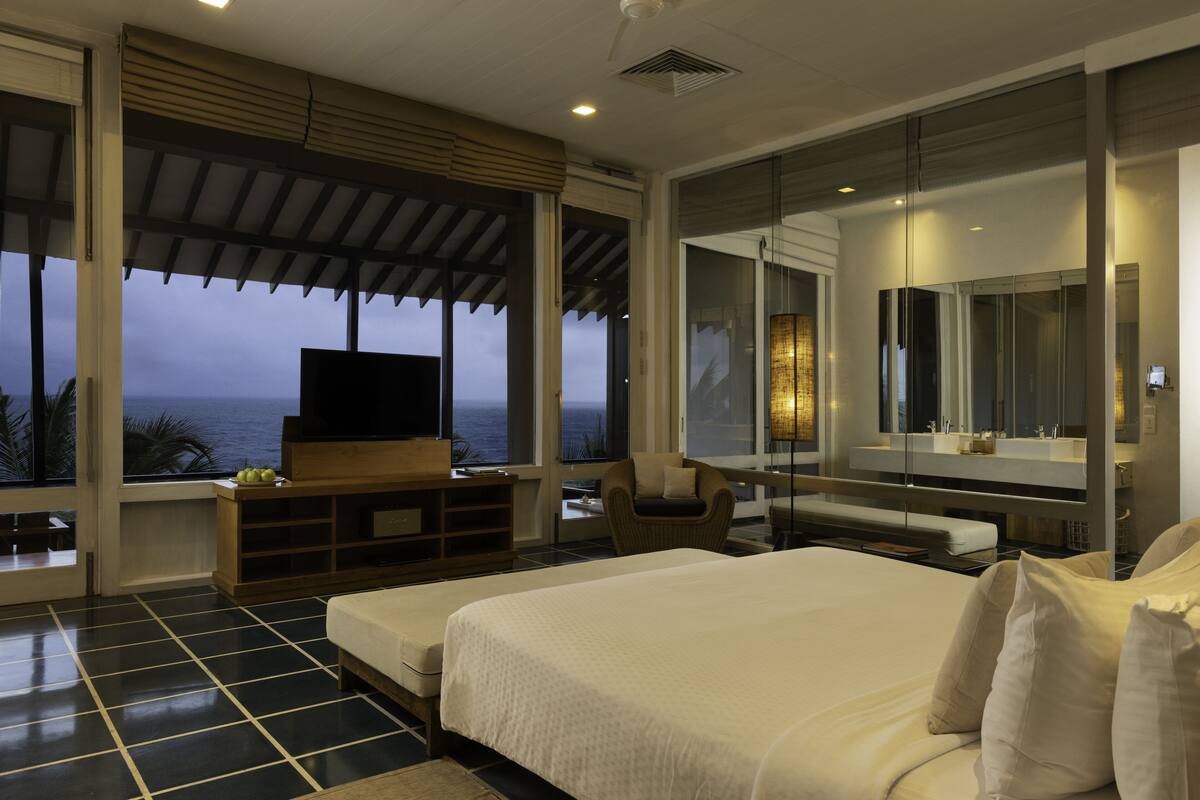 A bedroom with a large bed, a TV, a chair, and a view of the ocean.