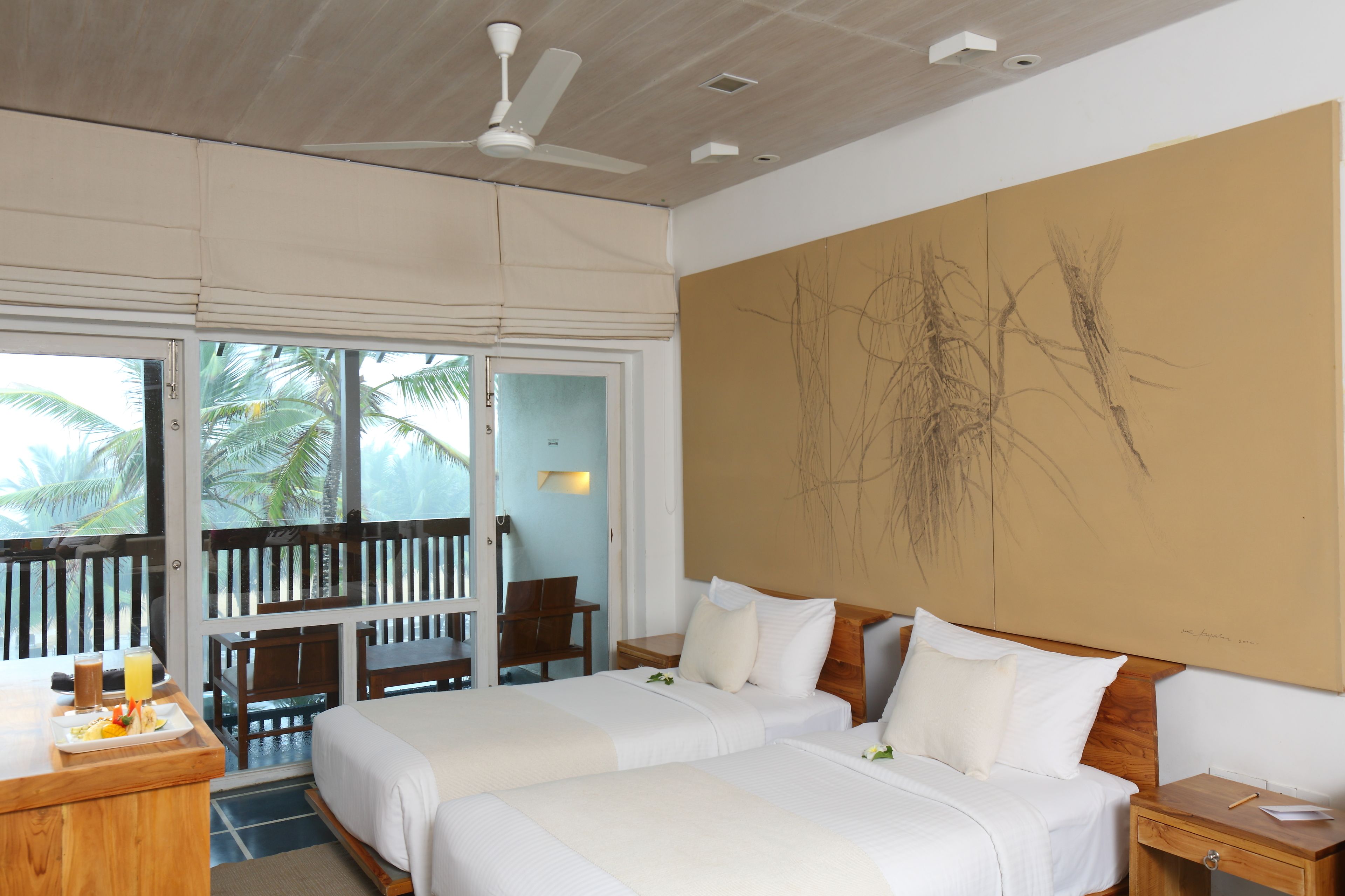 A hotel room with two beds, a balcony with a view of palm trees, a ceiling fan, and a large abstract painting on the wall.