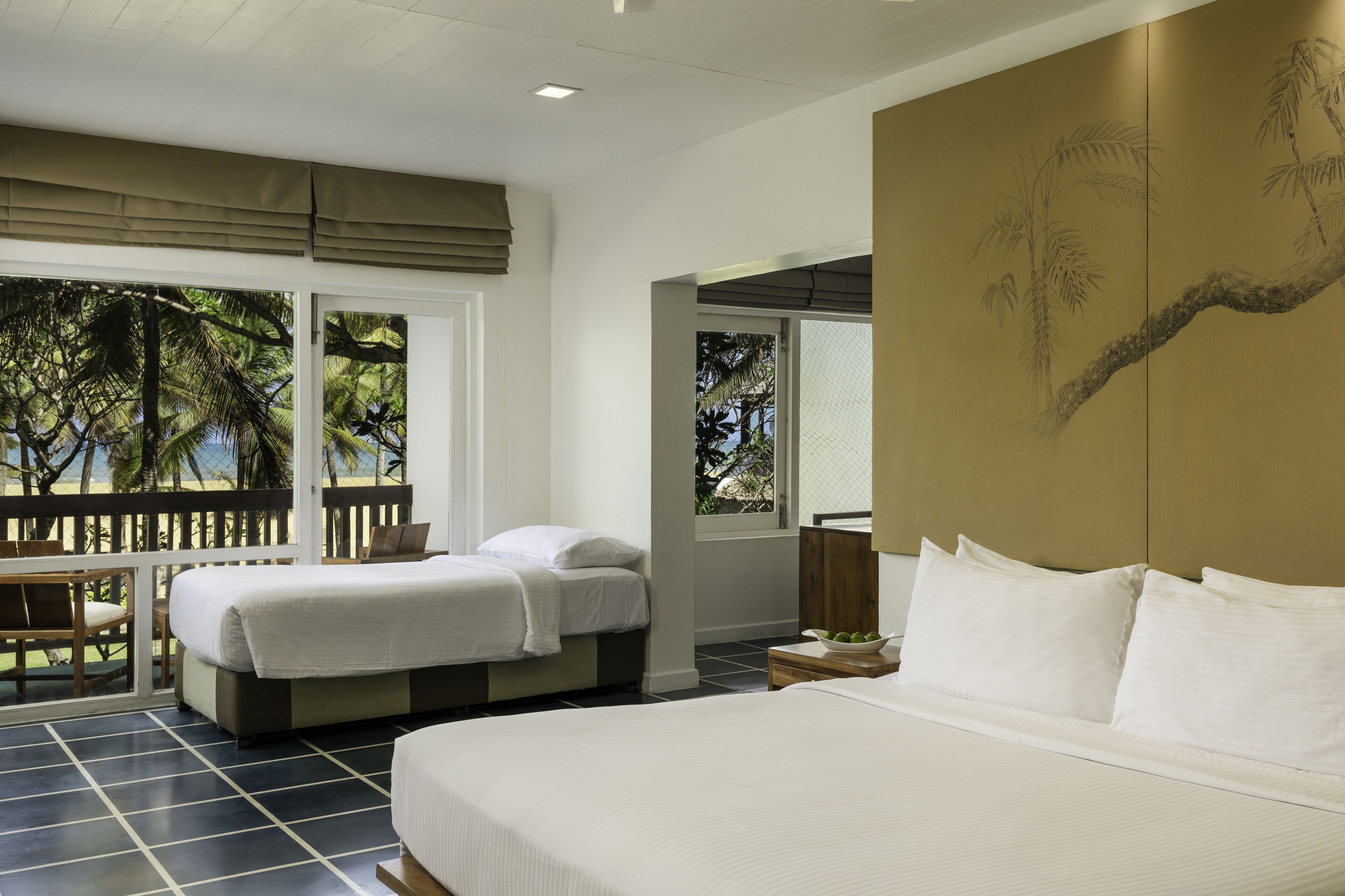 A hotel room with two beds, a large window with a view of palm trees, and a wooden bench outside.