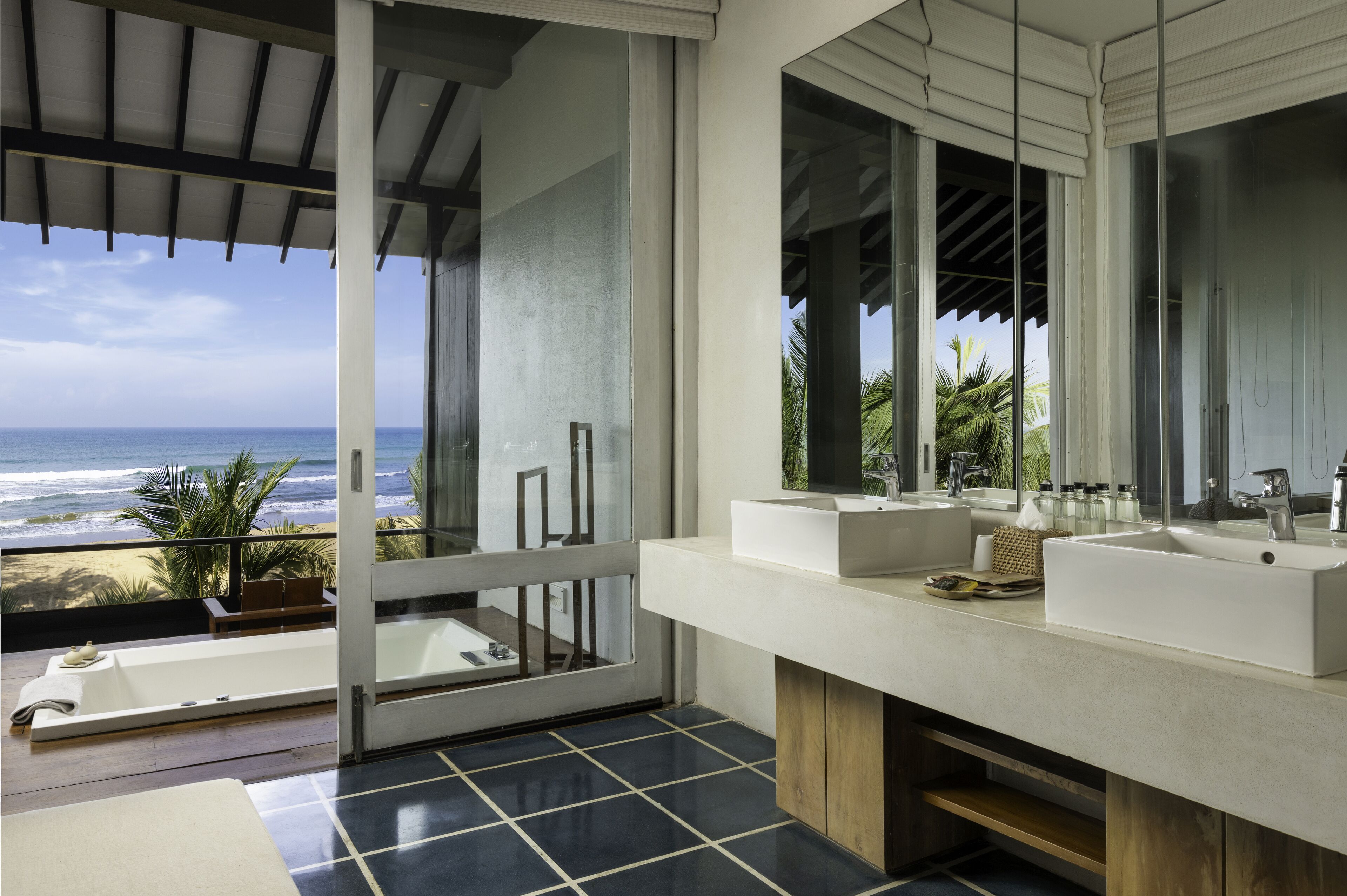 A modern bathroom with dual sinks, a large mirror, and a view of the ocean.