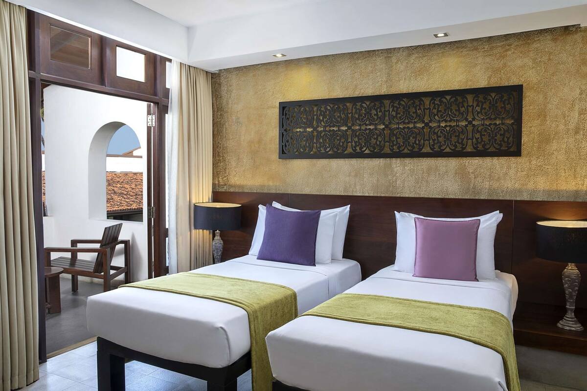 A hotel room with two beds, a view of the outside, and a decorative wall piece.