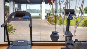 A treadmill and an elliptical machine in a room with a large window overlooking a body of water and palm trees. - Avani Kalutara Resort (Kalutara)