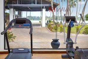 Un tapis de course et un appareil de musculation elliptique se trouvent dans une pièce dotée d’une grande fenêtre donnant sur un plan d’eau et des palmiers.