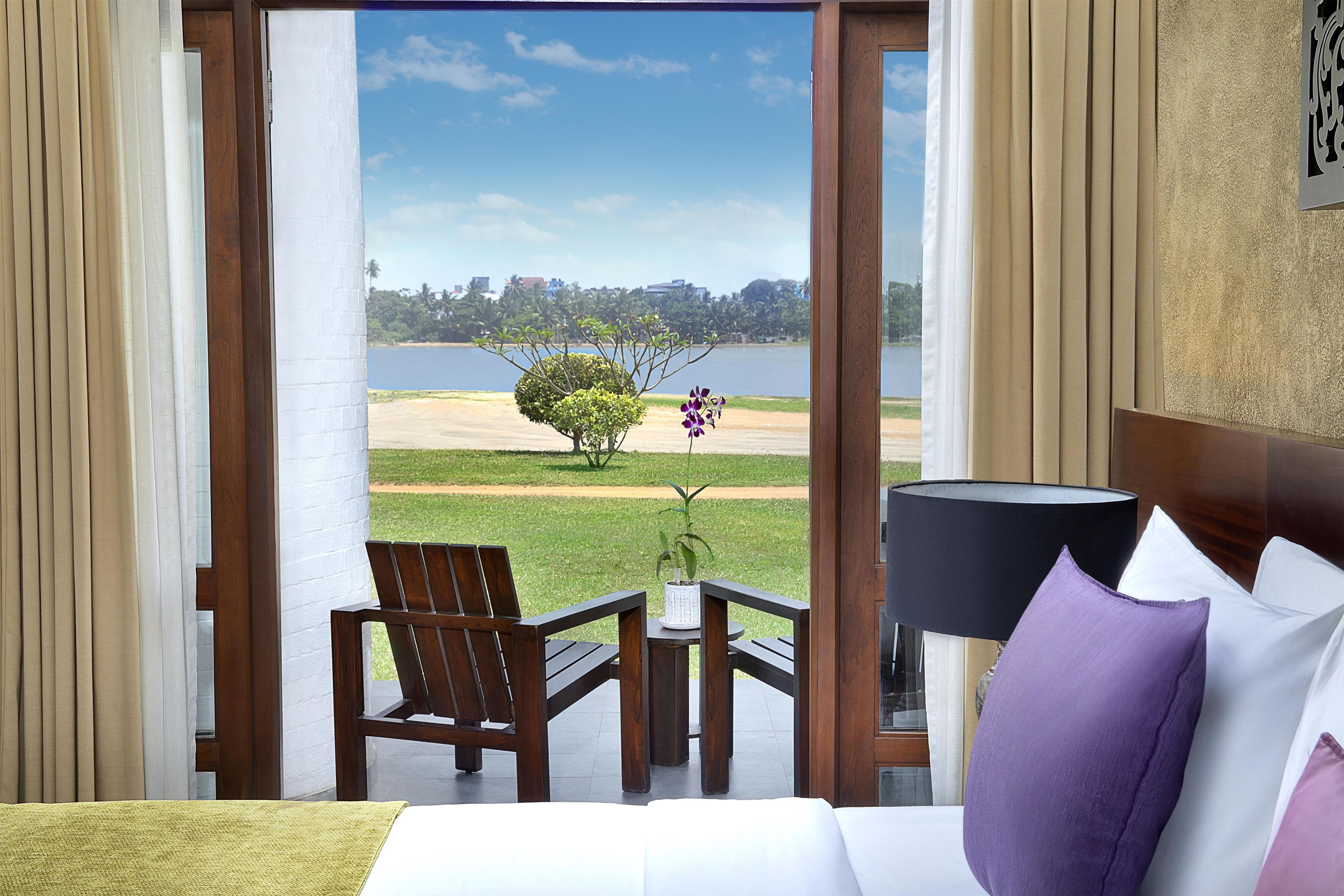 Habitación de hotel con cama, una mesa con sillas, vista a un lago y una lámpara.