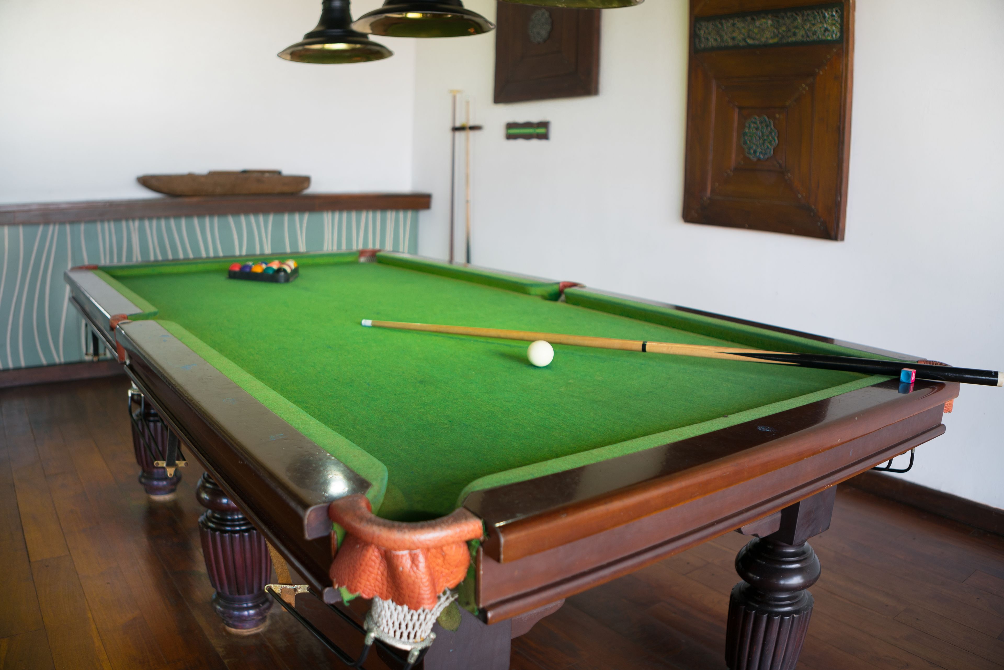 A pool table with a green felt surface, a white cue ball, and a pool cue.