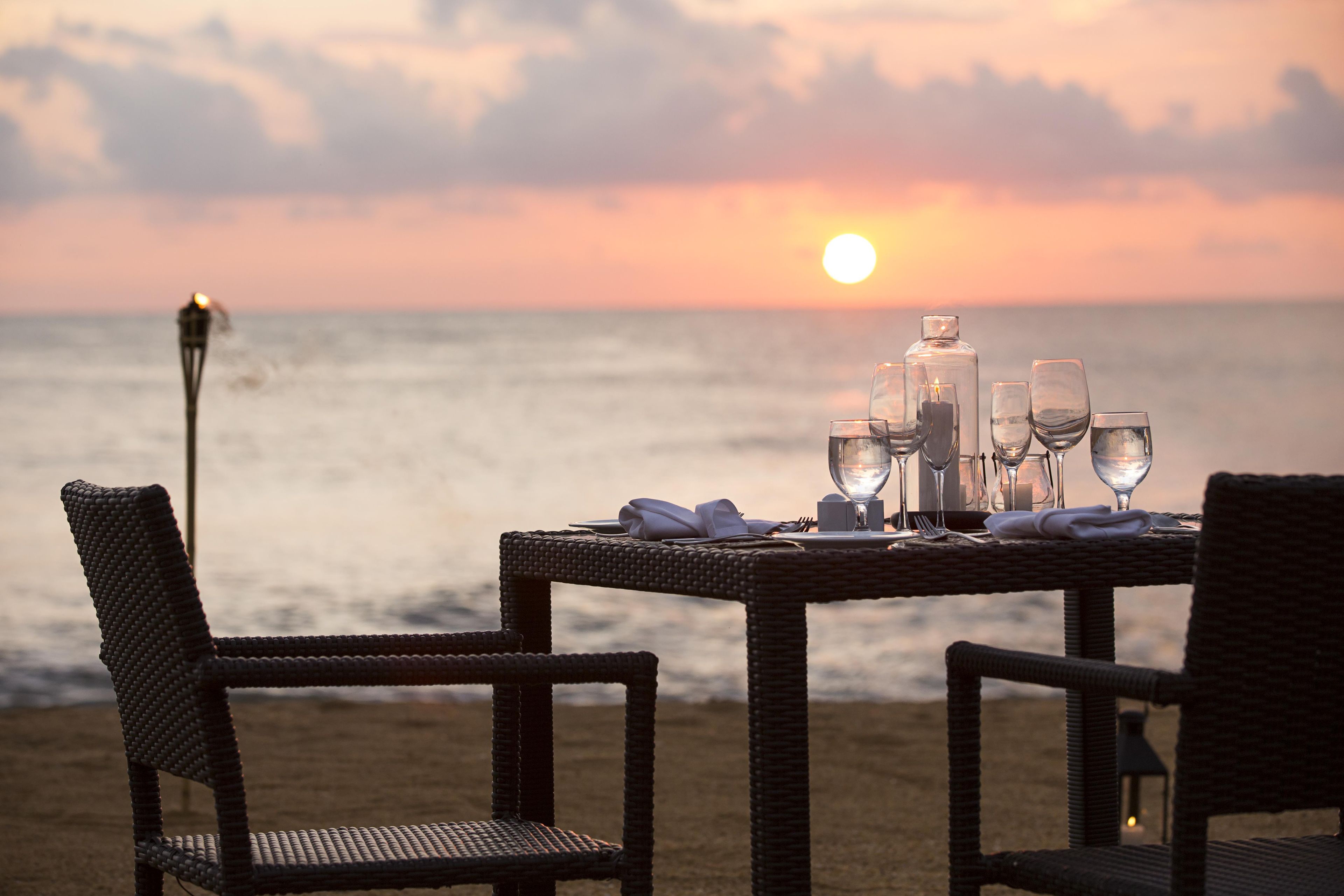 A table set for two with glasses and a bottle, overlooking the sea at sunset.