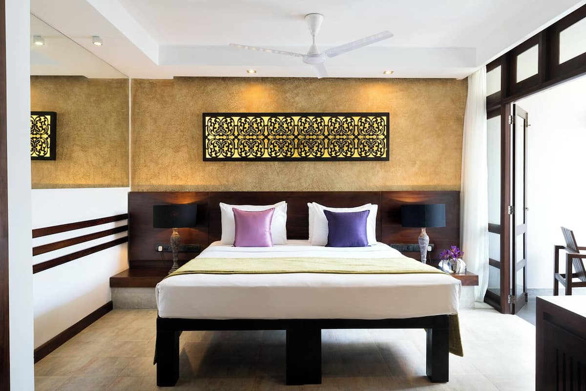 A hotel room with a large bed, a ceiling fan, and a decorative wall panel.