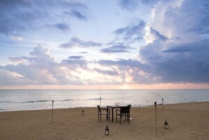 Uma praia com mesa e cadeiras montadas para refeições, um candeeiro e vista para o oceano.