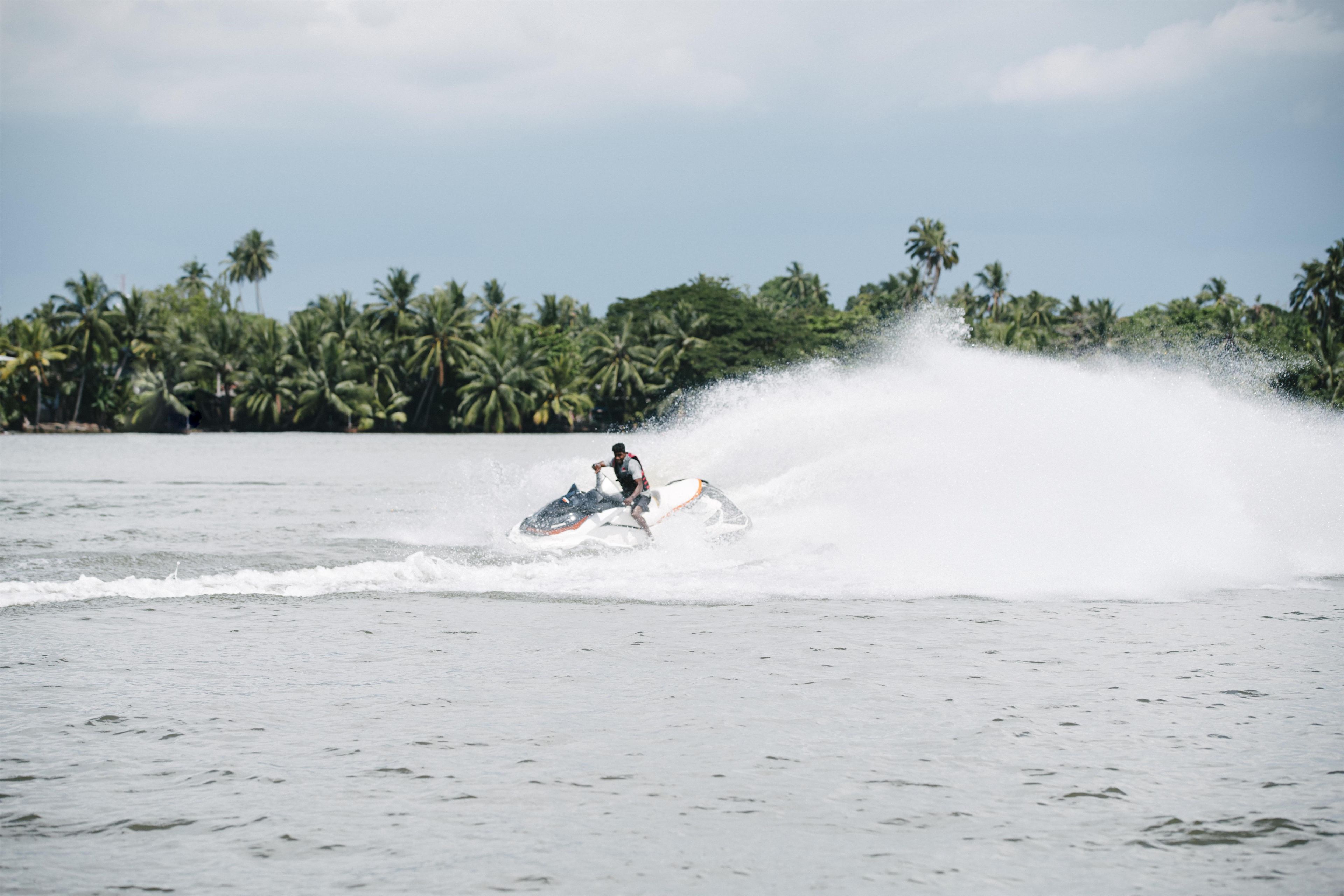 Una persona conduciendo un jet ski sobre el agua, con palmeras al fondo.