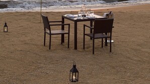 A table set on a sandy beach with chairs, a lantern, and a view of the ocean and sunset. - Avani Kalutara Resort (Kalutara)