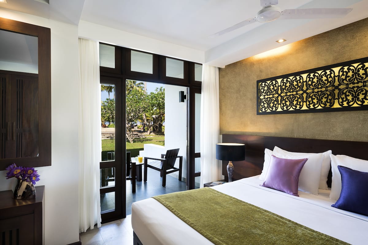 A hotel room with a bed, a nightstand, a lamp, and a view of the outdoors.