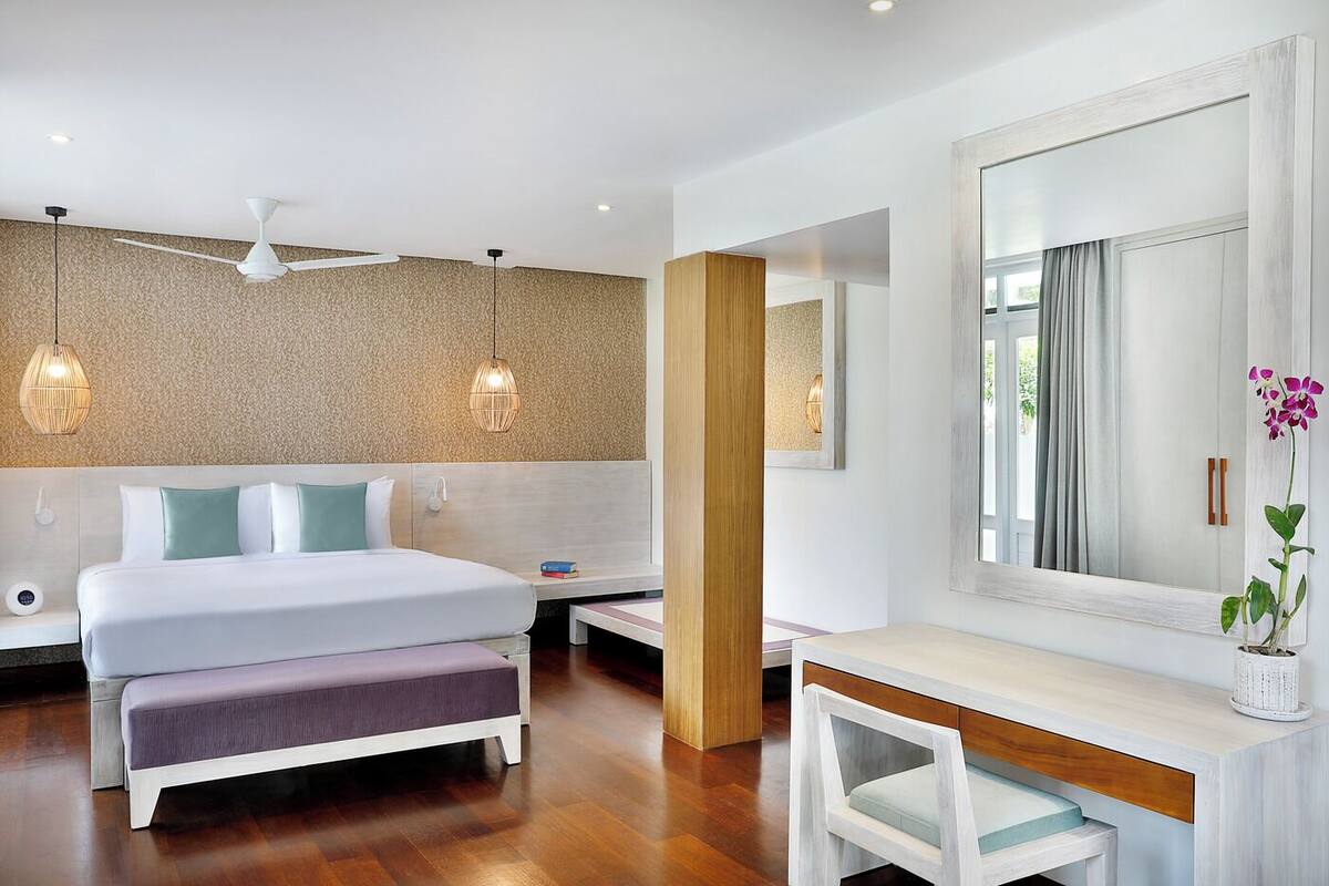 A modern hotel room with a large bed, bedside tables, a desk, and a mirror.