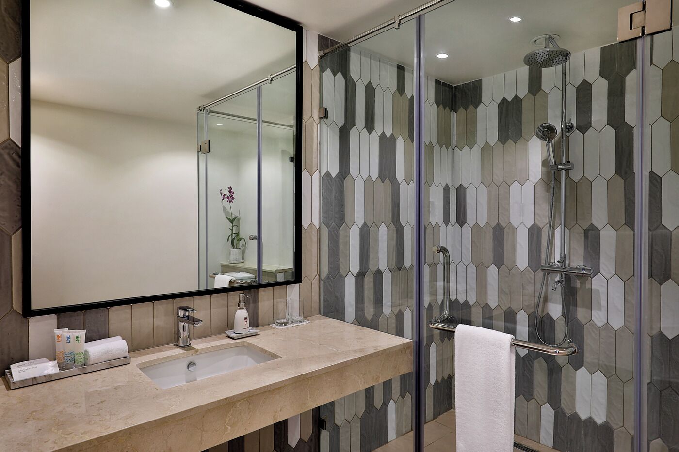 A modern bathroom with a large mirror, a sink, and a shower.