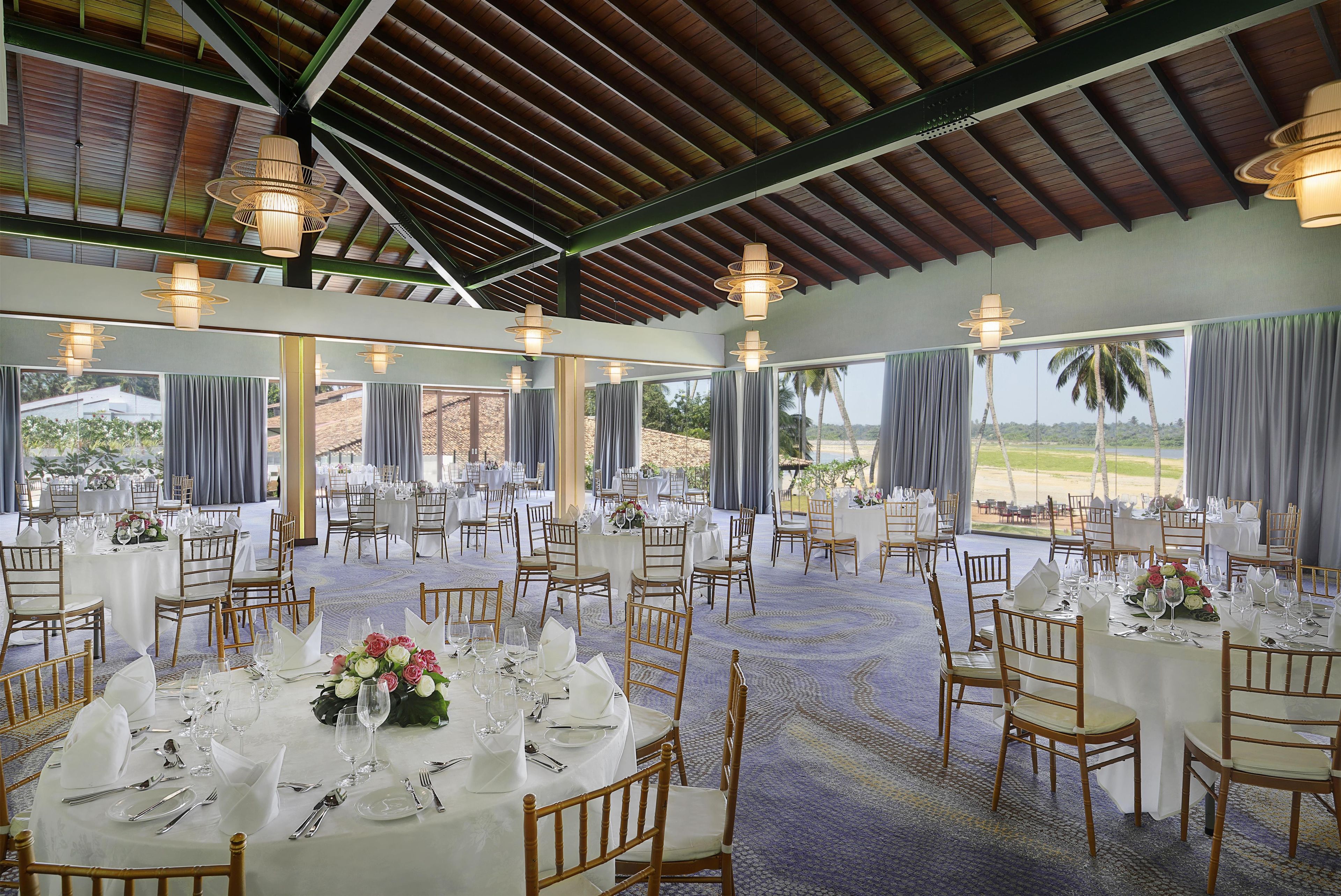 A banquet hall with round tables set for dining, large windows, and a view of palm trees.